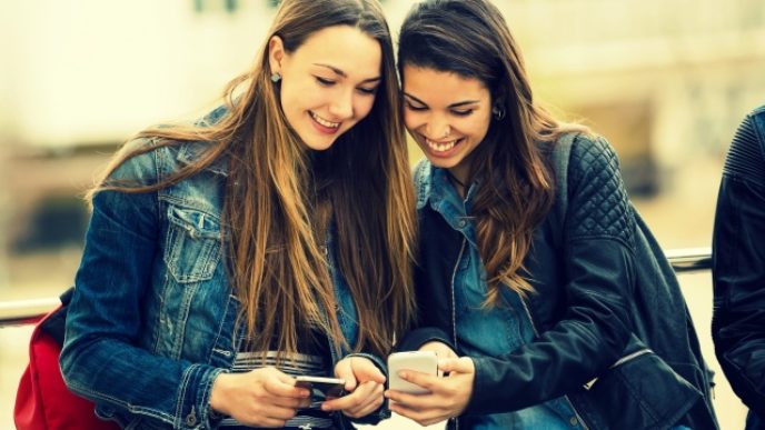 Portrait of two beautiful students using mobile phone in the street.