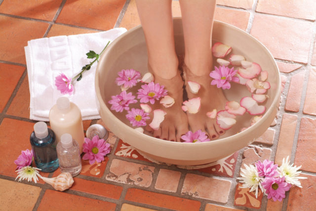 Feet stood in bowl of water with flowers next to lotions
