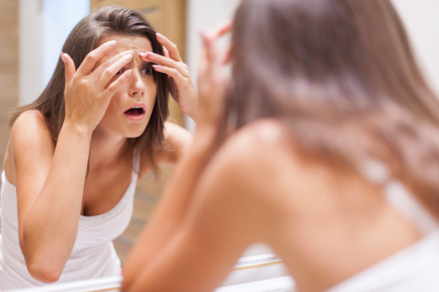 Shocked woman squeezing pimple in bathroom