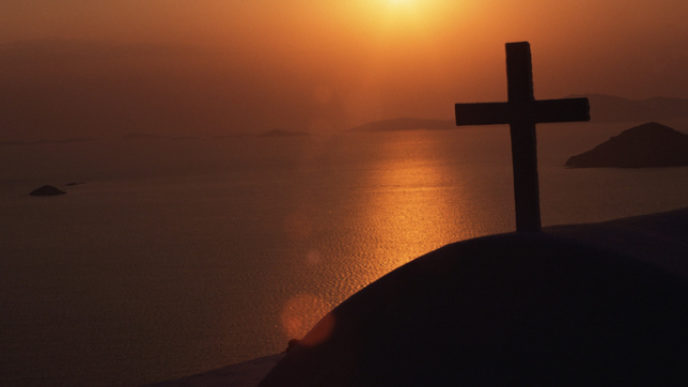 Silhouette of cross overlooking ocean at dusk