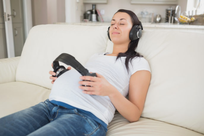 Pregnant woman holding headphones to belly and listening to music