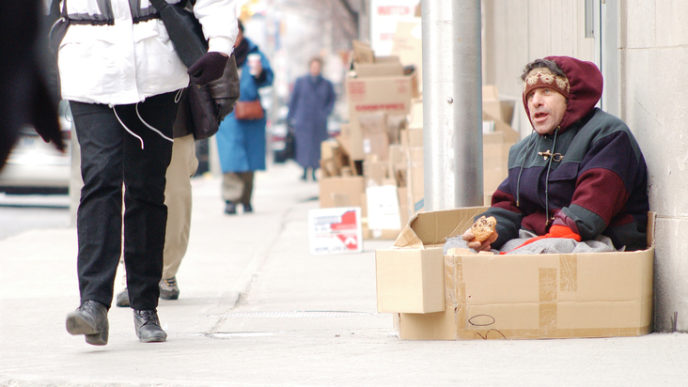 Pedestrians walking by homeless man on sidewalk