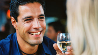 Close up of a man holding a glass of wine and smiling at a woman
