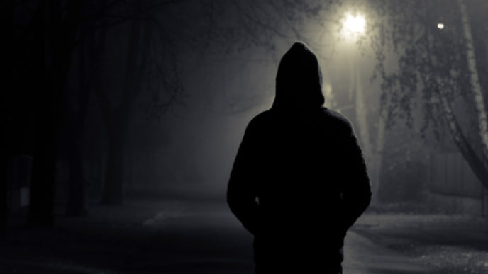 Silhouette of hooded person with spooky dark background