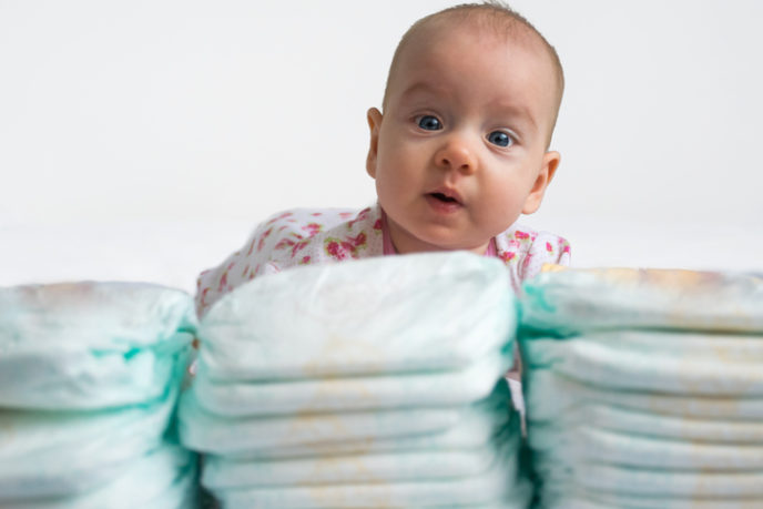 Baby looking over stack of diapers 1 v 2