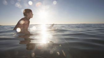 Teenage boy (15 17) in sea sitting on surfboard (sunflare)