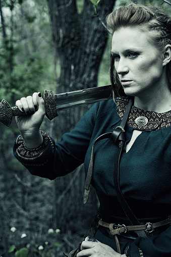 Brave scandinavian woman with sword posing in a forest