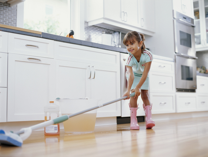 Girl (6 8) cleaning kitchen floor with mop, smiling, low angle view