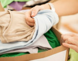 Female hands packing clothes into a donation box.