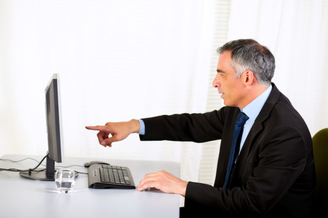 Muž sediaci za stolom ukazuje na monitor
