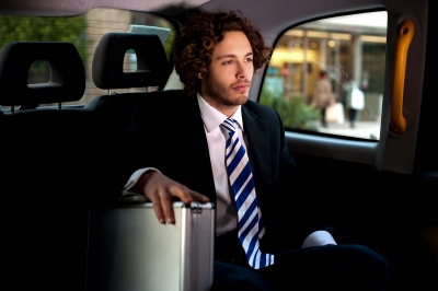 Muž v obleku s kufríkom sedí na zadnom sedadle auta