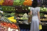 Woman holding bananas in produce aisle of supermarket, rear view