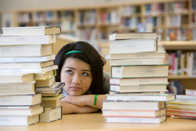 School girl (14 15) looking at stacks of books in library