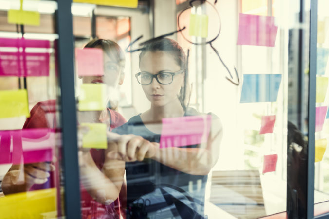 Two business women working together on wall glass