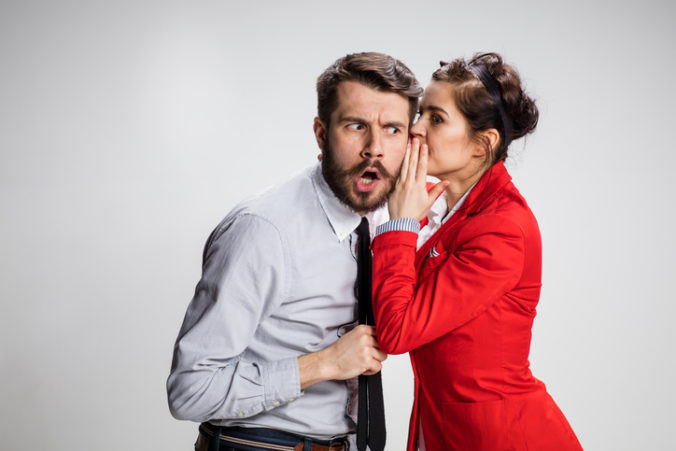 Young man telling gossips to his woman colleague at the