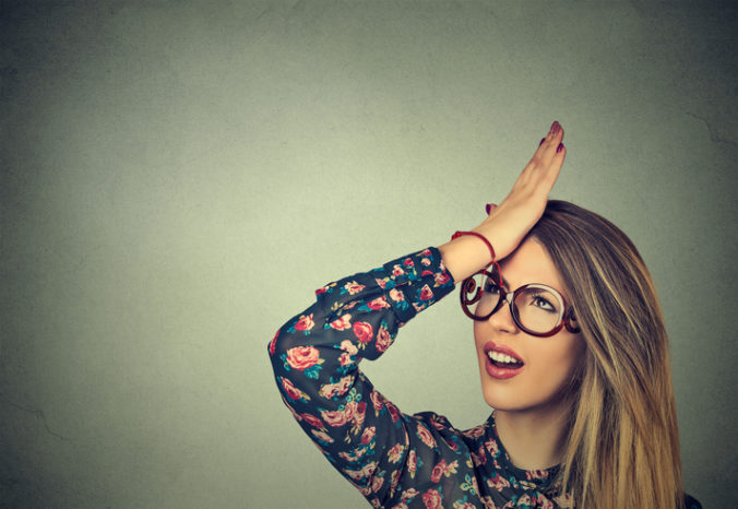 Silly woman slapping hand on head having duh moment