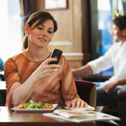 Woman sitting at table in bar, looking at mobile phone, smiling