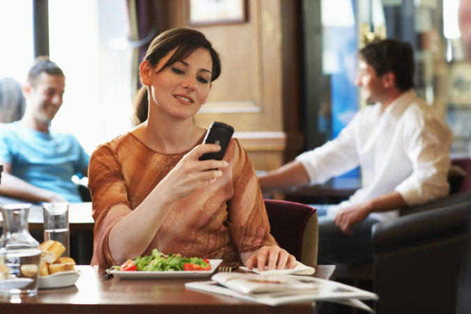 Woman sitting at table in bar, looking at mobile phone, smiling