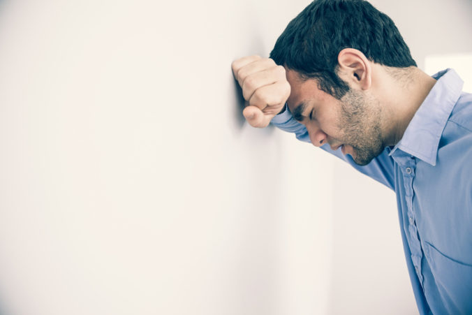 Depressed man leaning his head against a wall