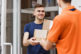 A person wearing an orange T shirt is delivering parcels to a satisfied client. Friendly worker, high quality delivery service