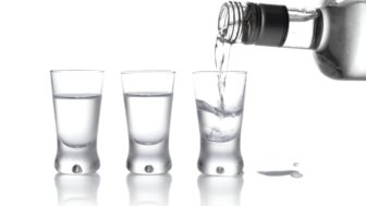 Láhev a sklenice vodky nalité do sklenice izolované na bílém podkladu