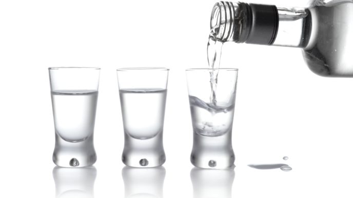 Láhev a sklenice vodky nalité do sklenice izolované na bílém podkladu
