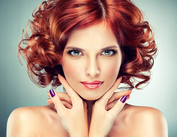 Beautiful model with red curly hair . Fashionable portrait , purple manicure