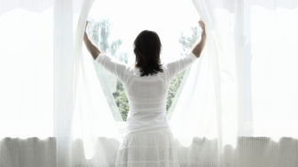 Woman opening curtains, looking out window, rear view