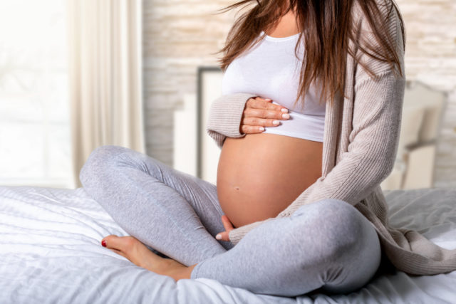 Closeup of a pregnant woman sitting on the bed