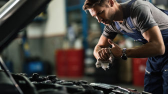Young auto mechanic cleaning hands after working on car engine in a garage.