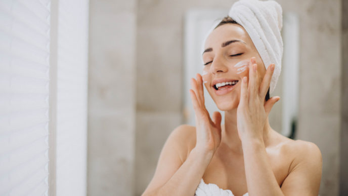 Young woman applying face cream on her face with towel on head