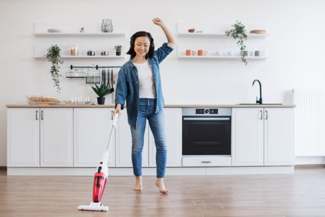 Woman getting floor clean with stick vacuum while dancing