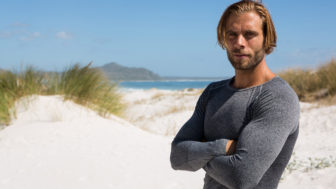 Portrait of confident athlete standing at beach against sky