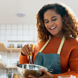 Young pretty African American woman enjoying herself cooking in kitchen while staying at home