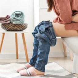 Young woman sitting on toilet bowl in restroom