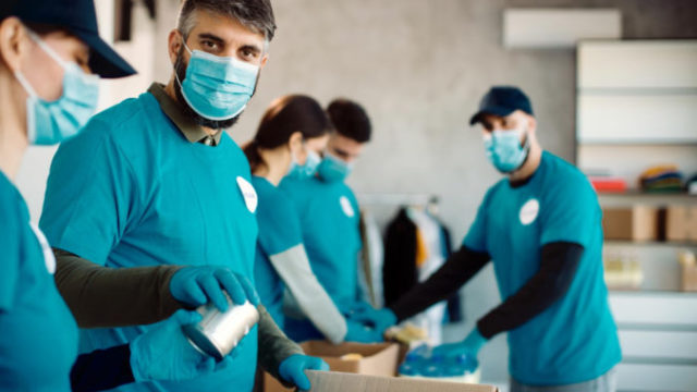 497691_group people with protective face masks packing donation boxes food charity 676x451.jpg