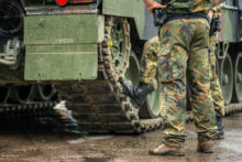 Two soldiers in camouflage uniform standing during a break under the rain near the tracks of an armoured tank