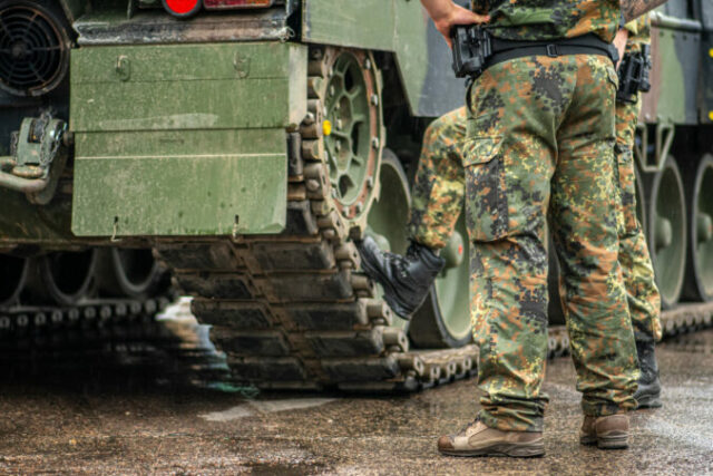 Two soldiers in camouflage uniform standing during a break under the rain near the tracks of an armoured tank