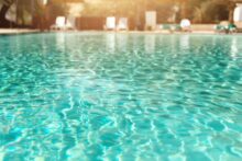 Summer, travel, vacation and holiday concept. Lounge chairs near swimming pool against Judean Desert. Turquoise pool with clean water, sun beds, greens of bamboo palms in tourist resort