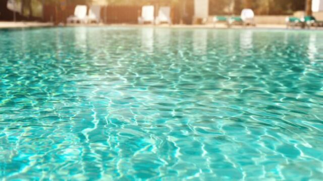 Summer, travel, vacation and holiday concept. Lounge chairs near swimming pool against Judean Desert. Turquoise pool with clean water, sun beds, greens of bamboo palms in tourist resort