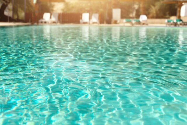 Summer, travel, vacation and holiday concept. Lounge chairs near swimming pool against Judean Desert. Turquoise pool with clean water, sun beds, greens of bamboo palms in tourist resort