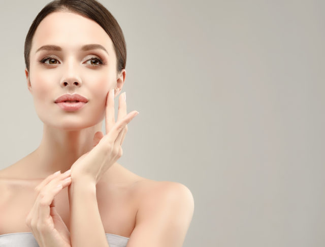 Gorgeous, young woman with clean, fresh skin is touching own face. Cosmetology.