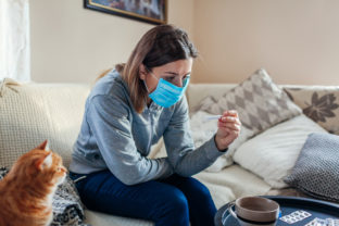 Ill woman checking thermometer having fever. Girl wearing protective mask while having cold, flu at home. Healthcare