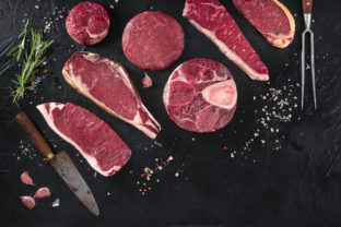 Various cuts of meat, shot from the top on a black background with salt, pepper, rosemary and knives, with copy space