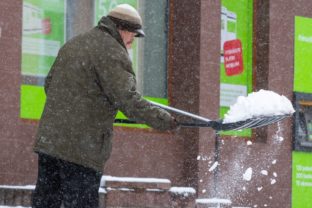 Muž odhàňa sneh zo zasneženého chodníka počas hustého sneženia na Námestí svätého Egídia v Poprade. Poprad, 6. apríl 2021.
