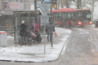 Pohľad na ľudí na autobusovej zastávke Cintorín Slávičie údolie počas sneženia v Bratislave. Bratislava, 26. november 2021