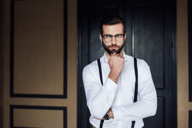 Thoughtful elegant man posing in white shirt and suspenders