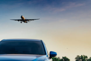 Commercial airline. Passenger plane landing approach blue SUV car at airport with blue sky and clouds at sunset. Arrival flight. Vacation time. Happy trip. Airplane flying on bright sky. Car parked.