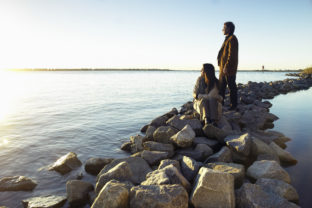 Mature couple watching sunrise on rock breakwater