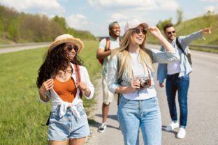 Group of positive young friends walking along highway, making photos, having fun together outdoors